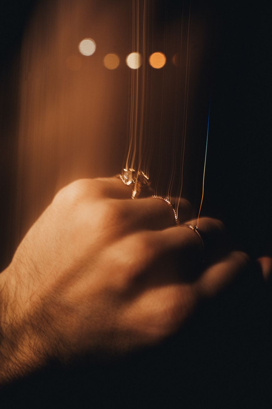 A blurred, artistic close-up of a man's hand adorned with rings, captured in low light for a dramatic effect.