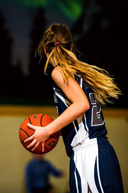 Free Woman in Blue and White Basketball Jersey Holding Brown Basketball Stock Photo