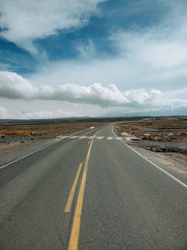 Empty road stretching into the distance under a vibrant blue sky with fluffy clouds.