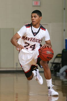 A young male basketball player dribbles on an indoor court wearing a Maverick jersey.
