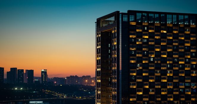 Capture of a modern city skyline at dusk with illuminated buildings and a vibrant sunset.