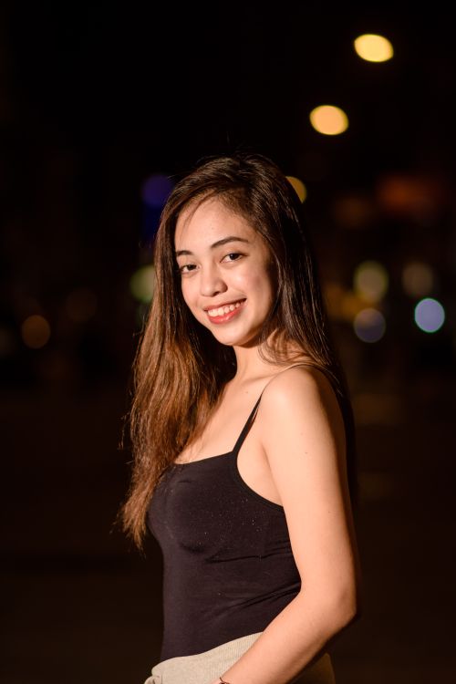 Free A young woman with long hair smiling in a nighttime urban environment, captured in portrait style. Stock Photo