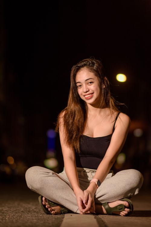 Free Young woman sitting cross-legged at night in city street, exuding casual and happy vibes. Stock Photo