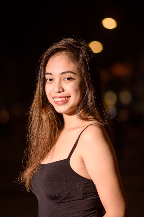 Free Portrait of a confident young woman in a black top, smiling brightly against a night backdrop. Stock Photo