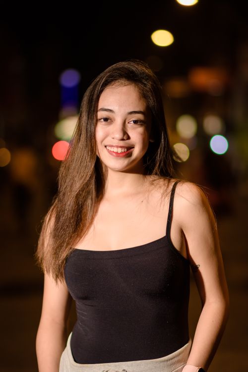 Free A young woman in a black top smiling outdoors at night with blurred lights. Stock Photo