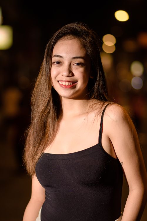 Free Young woman smiling on city street at night, wearing a black top. Urban portrait captures a lively mood. Stock Photo