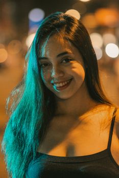 Portrait of a woman with long hair smiling outdoors at night in an urban setting.