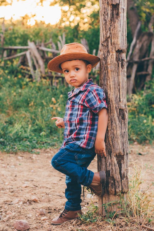 A Little Boy in a Cowboy Outfit Standing against a Tree on a Farm 