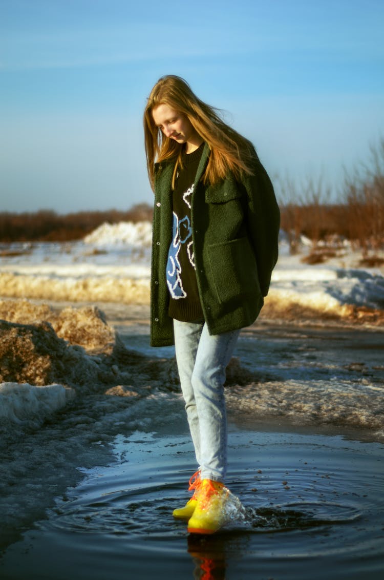 Young Woman Standing In A Puddle On A Snowy Field 