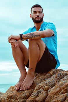 Man sitting barefoot on coastal rocks, enjoying a calm summer day by the sea.
