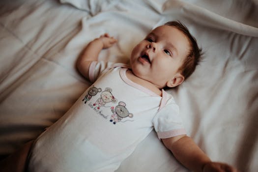 Smiling baby wearing a cute onesie lying comfortably on a white bed indoors.
