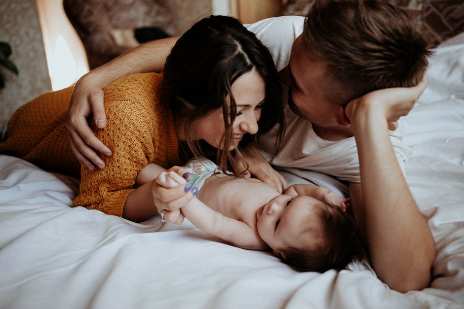 A joyful family moment with parents playing with their baby on a bed, highlighting love and connection.