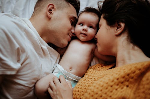 Free Parents Lying on the Bed with Their Newborn Baby Stock Photo
