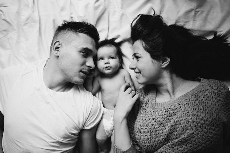 Black And White Photo Of Baby Lying Between Parents