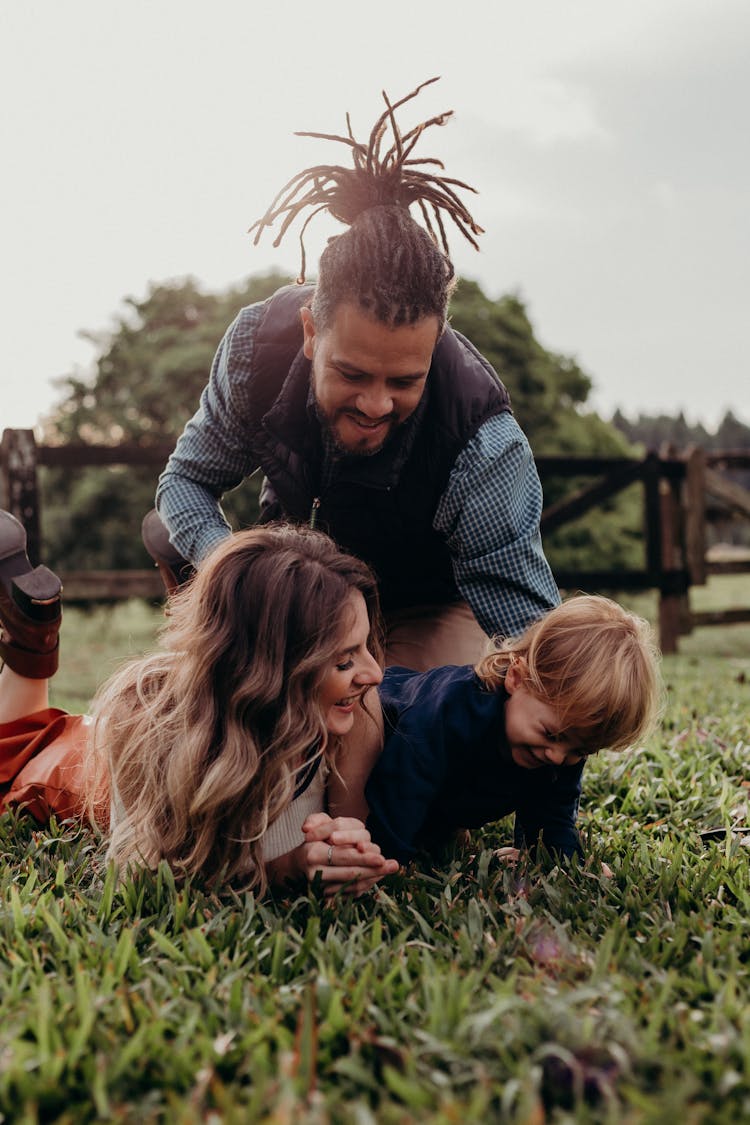 Parents And Their Little Son Lying On The Grass Outdoors And Laughing 