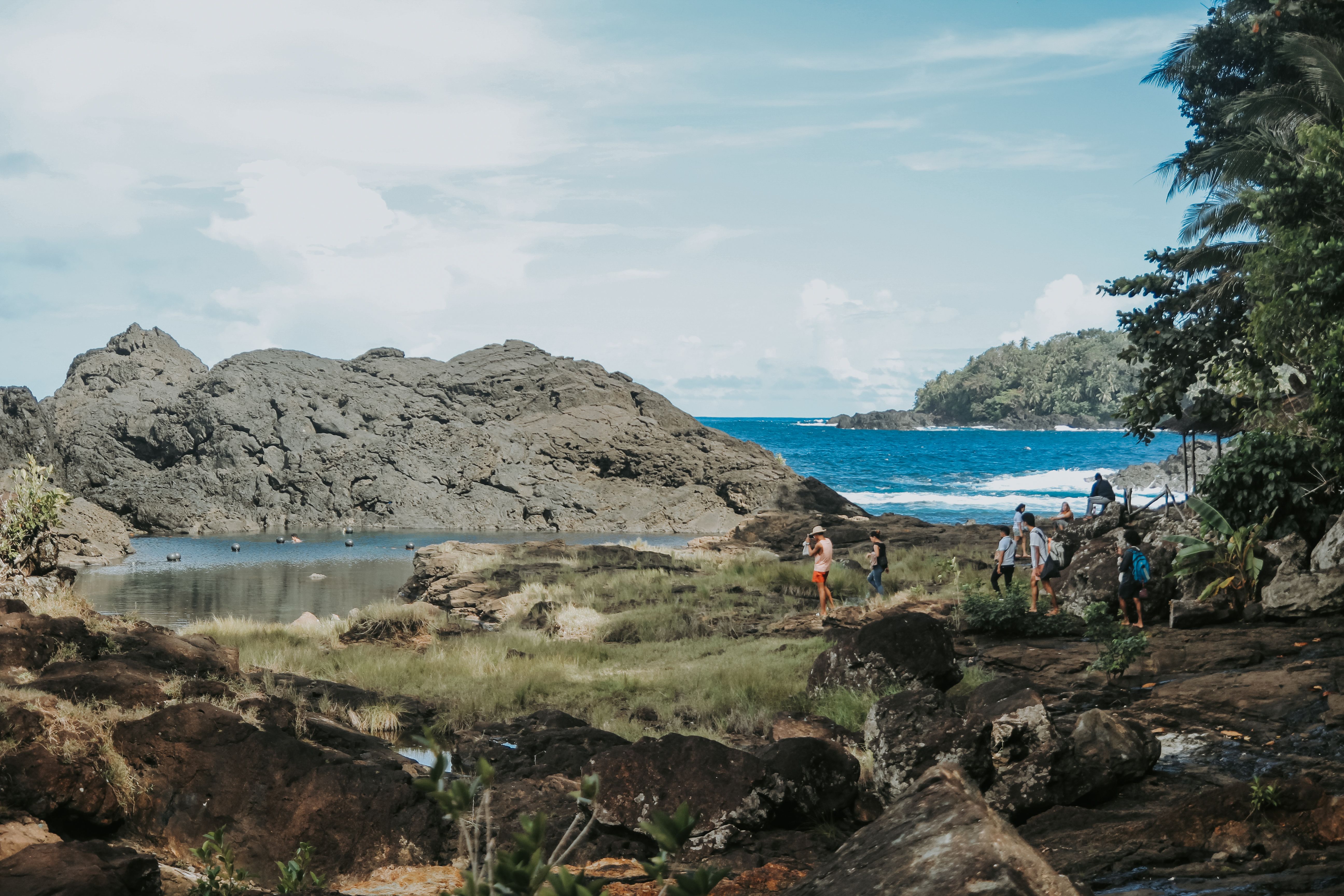 Tourists explore a stunning rocky coastal landscape under a bright sky.