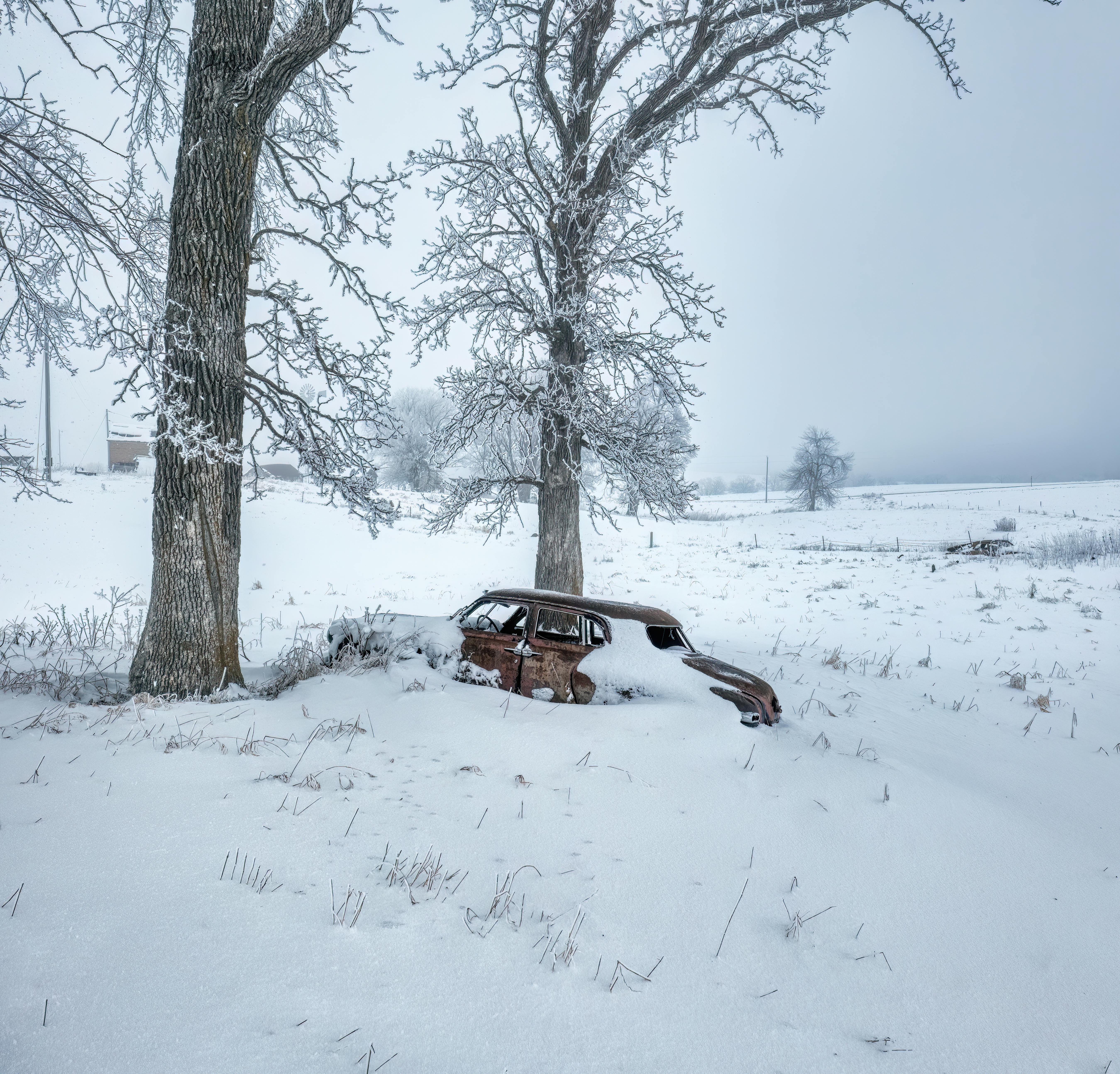 Rustic car buried in snow amidst a winter landscape in rural Minnesota.