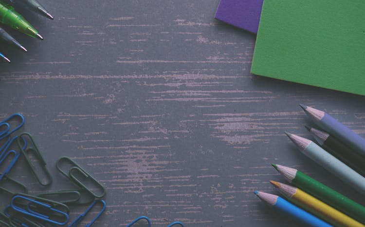 Colored Pencils On A Gray Desk With Paper Clips And Folders