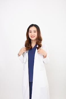 Professional female doctor in scrubs and lab coat smiling confidently on white background.