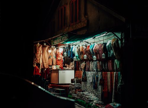 Free A colorful street stall displaying an array of textiles and dresses at night in an urban market. Stock Photo