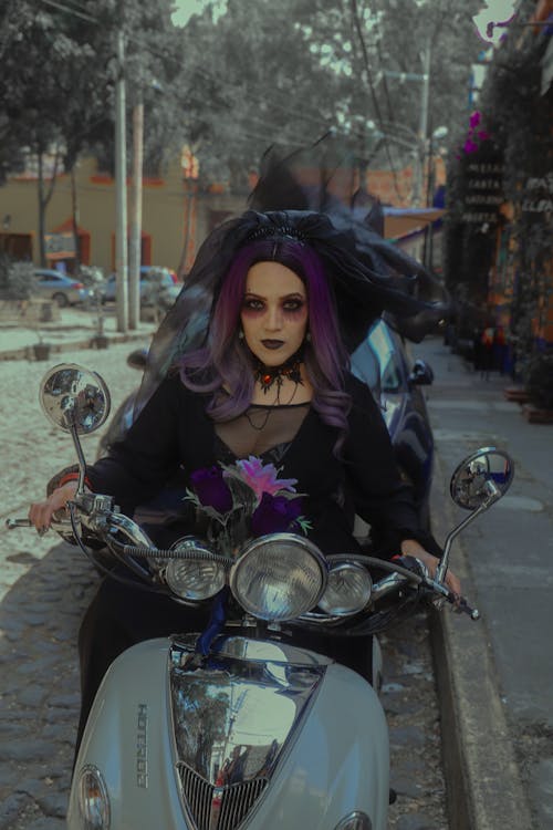 Woman in a Halloween Costume, Makeup and a Purple Wig Sitting on a Motor Scooter 