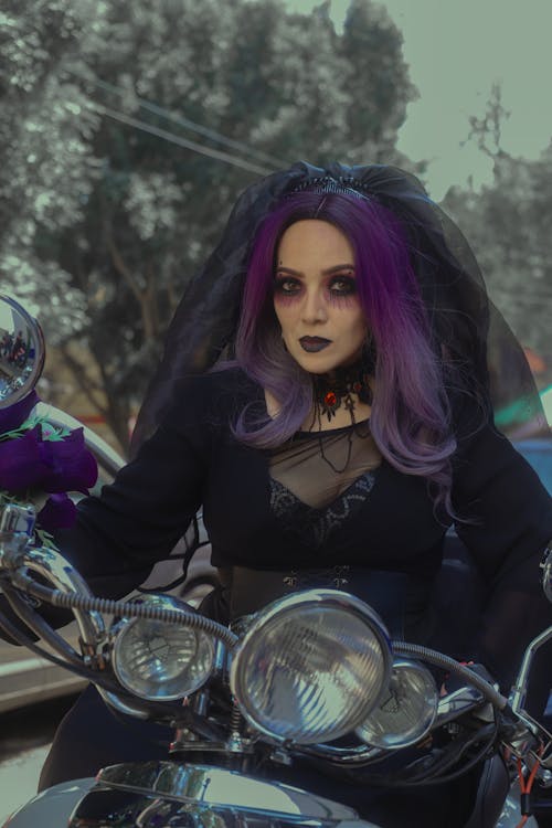 Woman in a Halloween Costume, Makeup and a Purple Wig Sitting on a Motor Scooter 