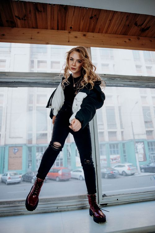 Free Fashionable young woman posing in a city wearing a puffer jacket and distressed jeans. Stock Photo
