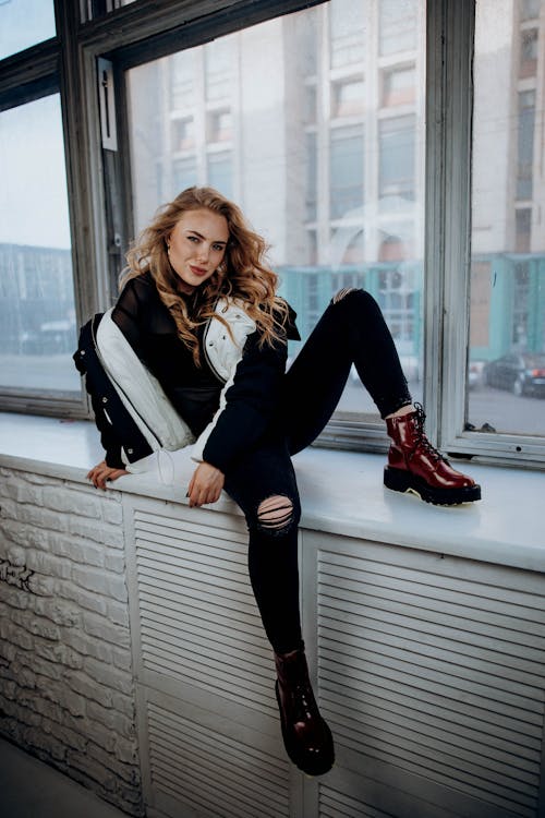 Model Posing in Distressed Jeans and Boots Sitting on a Window