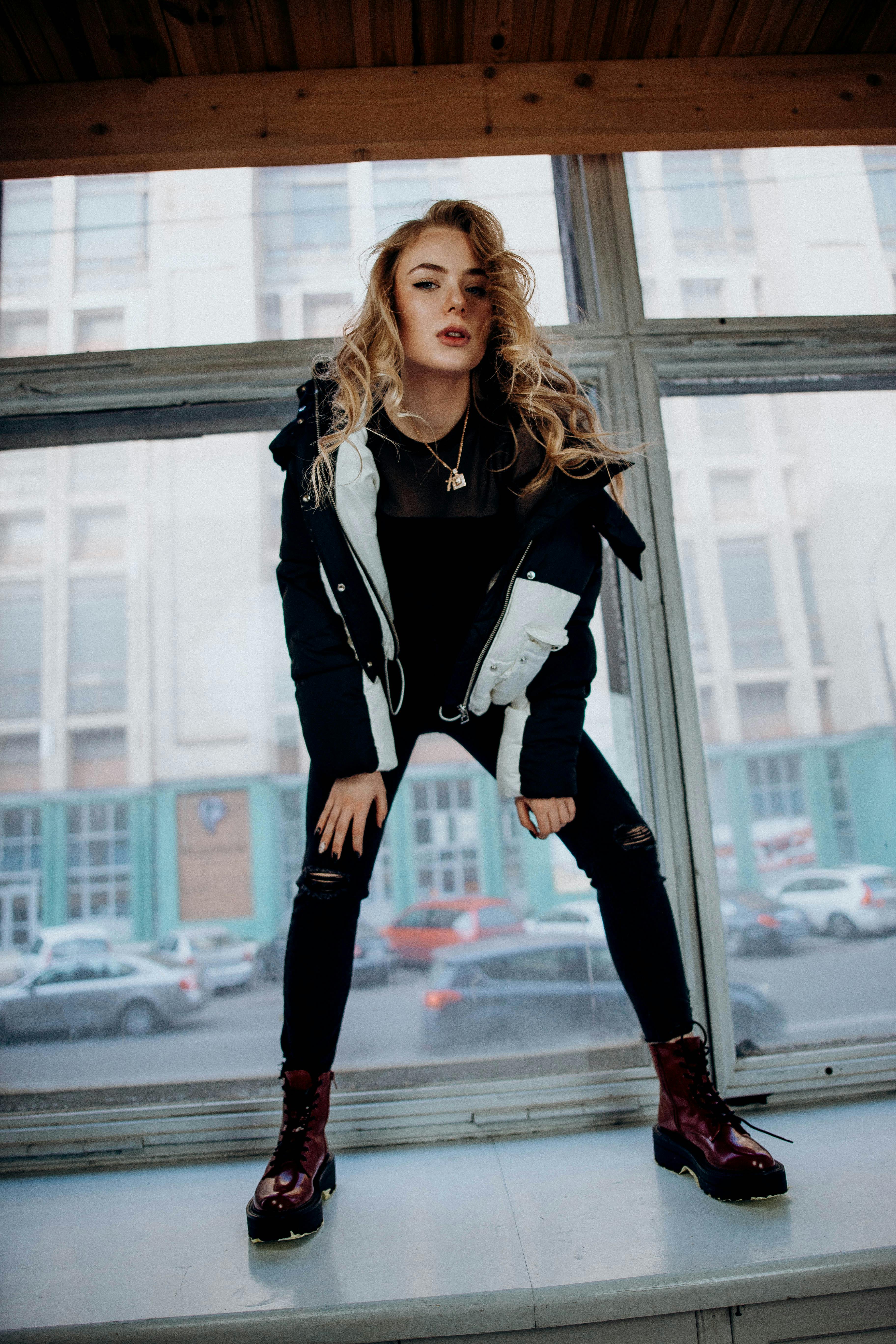 Free Dynamic fashion portrait of a young woman posing by a windowsill in an urban environment. Stock Photo