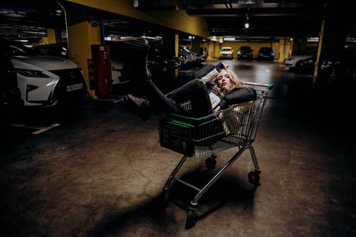 Free A woman poses with confidence in a shopping cart inside a dimly lit parking garage. Stock Photo