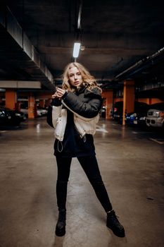 Fashionable woman posing confidently in a dimly lit urban parking lot, showcasing street style.