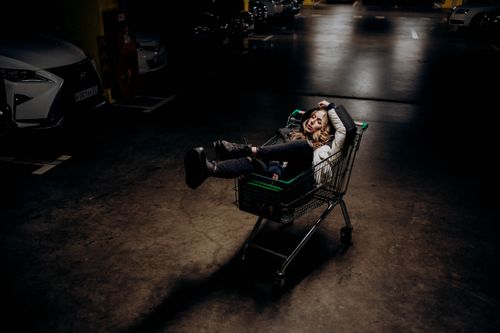 Free A woman lies in a shopping cart in a dimly lit parking garage, conveying urban exploration. Stock Photo