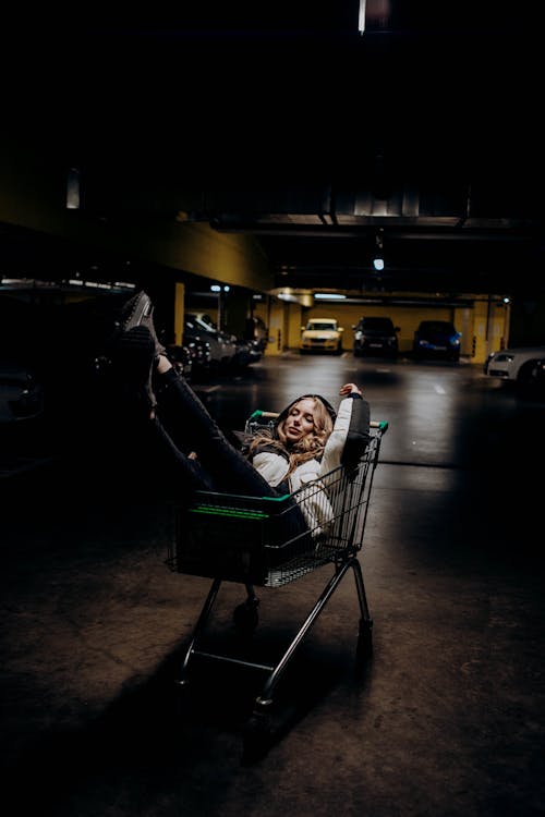 Young Woman Sitting in a Shopping Cart on an Underground Parking Lot 