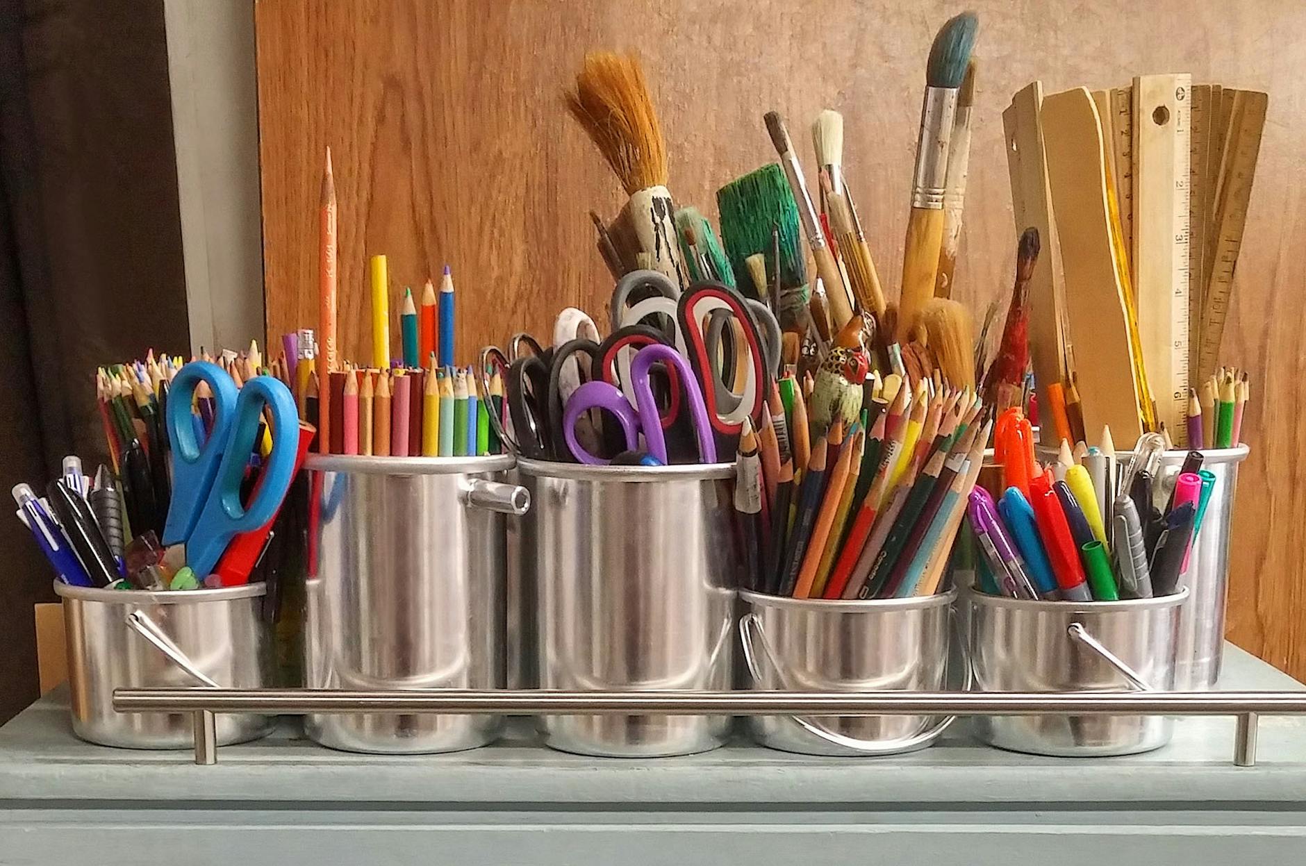 prateleira com diversos potes cheios de lápis coloridos, tesouras, pincéis e réguas em sala de aula