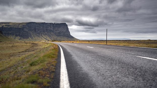 A remote Icelandic highway with stunning cliffs under a cloudy sky, perfect for adventure travel.
