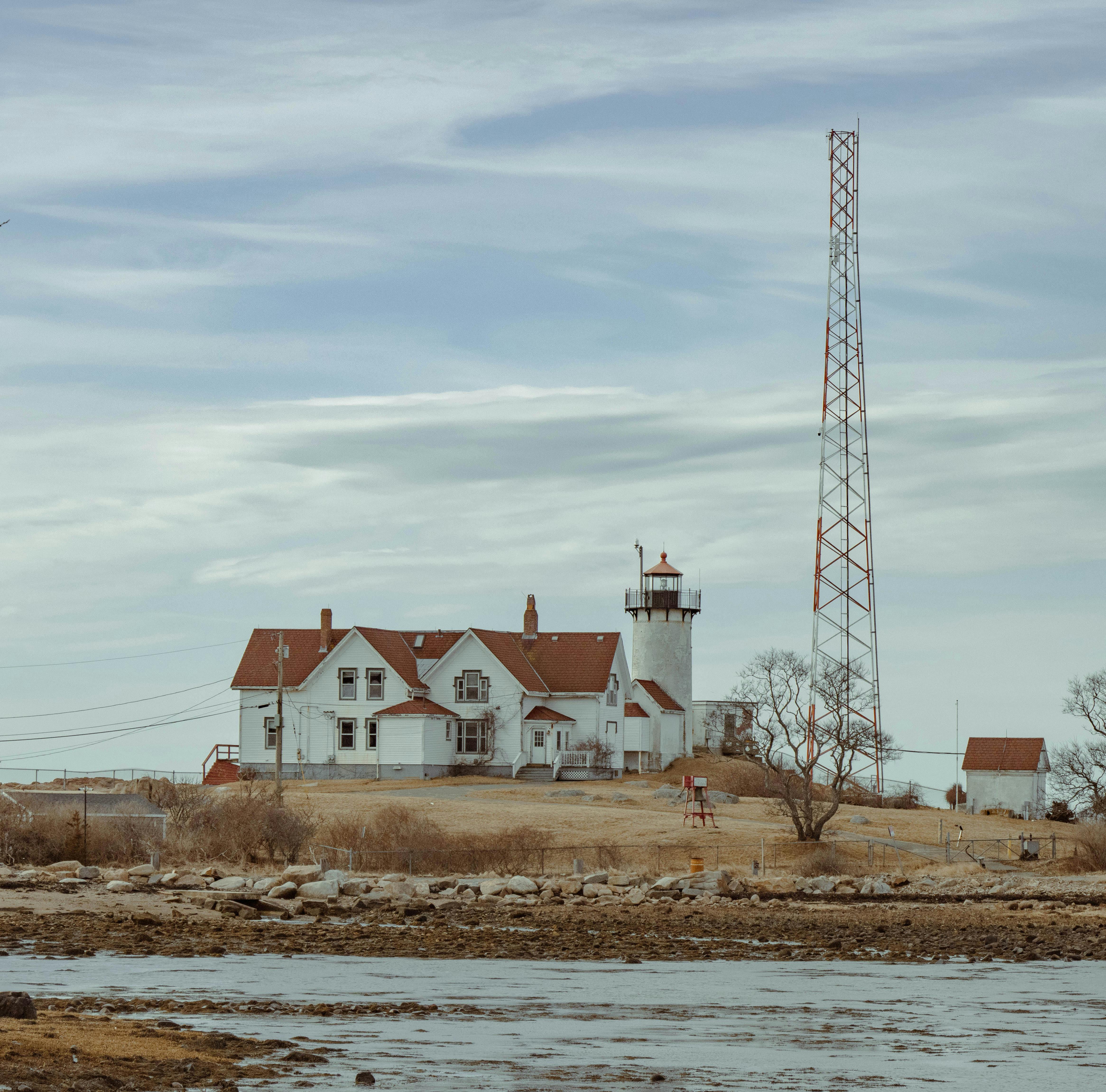 Charming coastal lighthouse with adjacent house, blue sky, and coastal scenery.