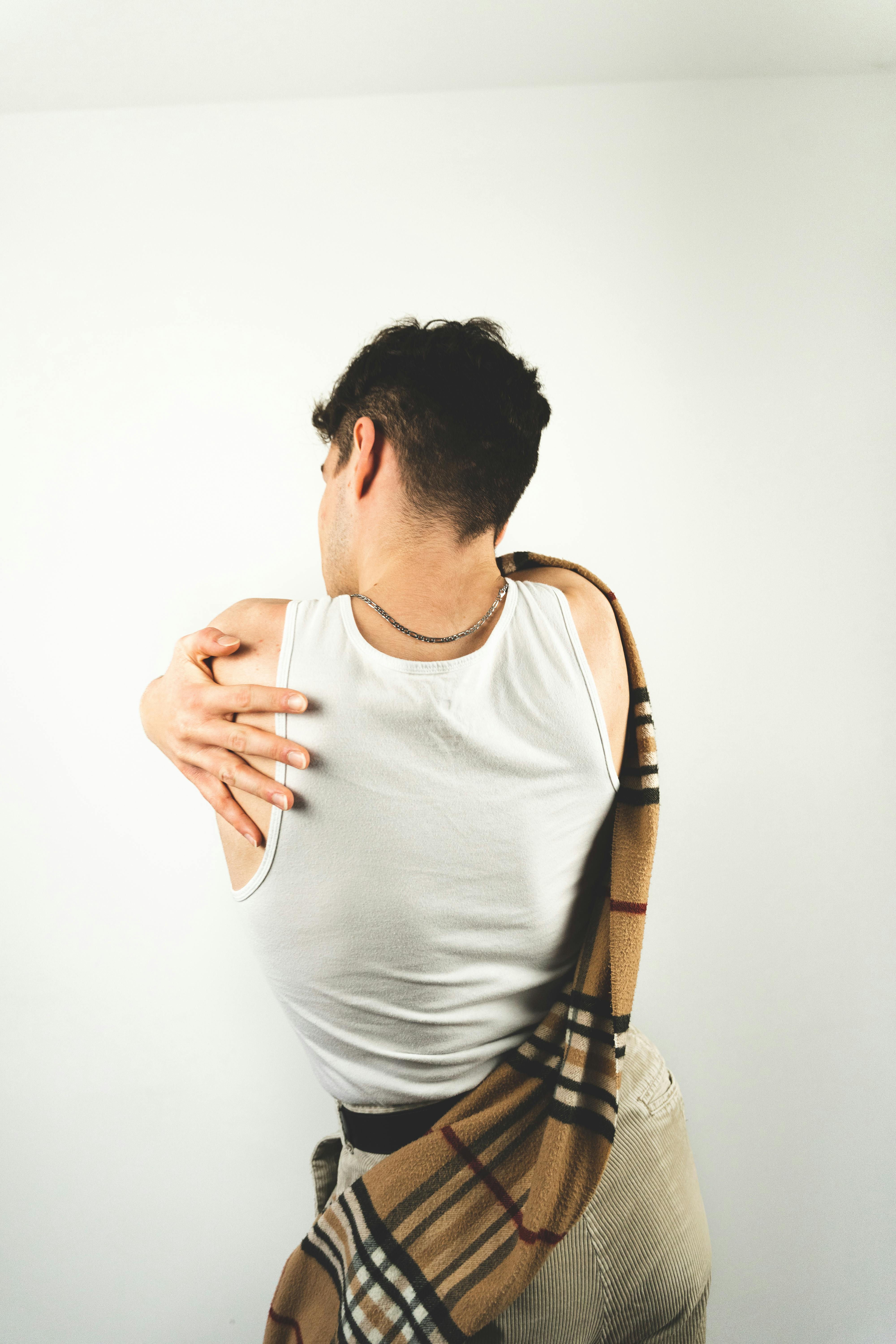 A man with short black hair in a white tank top stands against a white backdrop.
