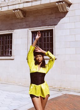 Fashionable woman in yellow shirt and black corset posing in sunlight outside a building.