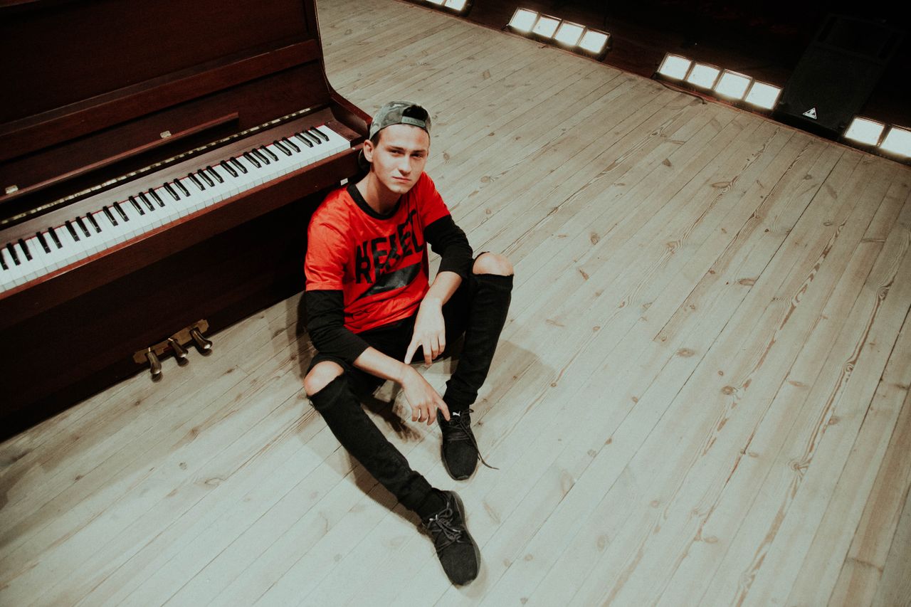 teen sitting casually by a piano in a studio setting expressing youthf