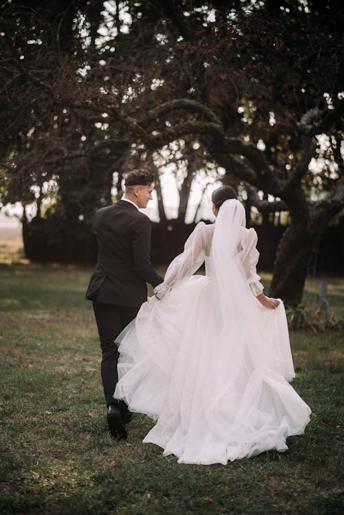 Back View of Bride and Groom Holding Hands and Walking in the Garden