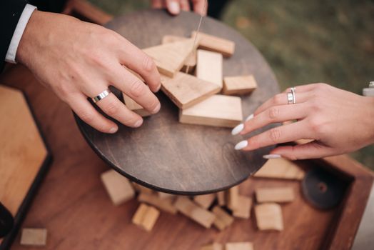 Close-up of hands playing with wooden blocks featuring wedding rings at a reception.