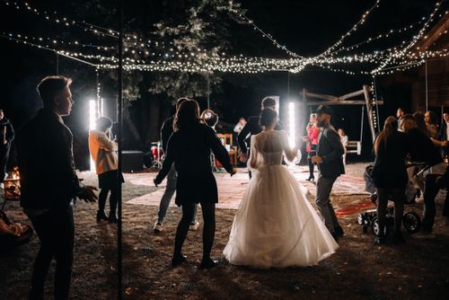 Free A lively outdoor wedding reception with guests dancing under string lights at night. Stock Photo