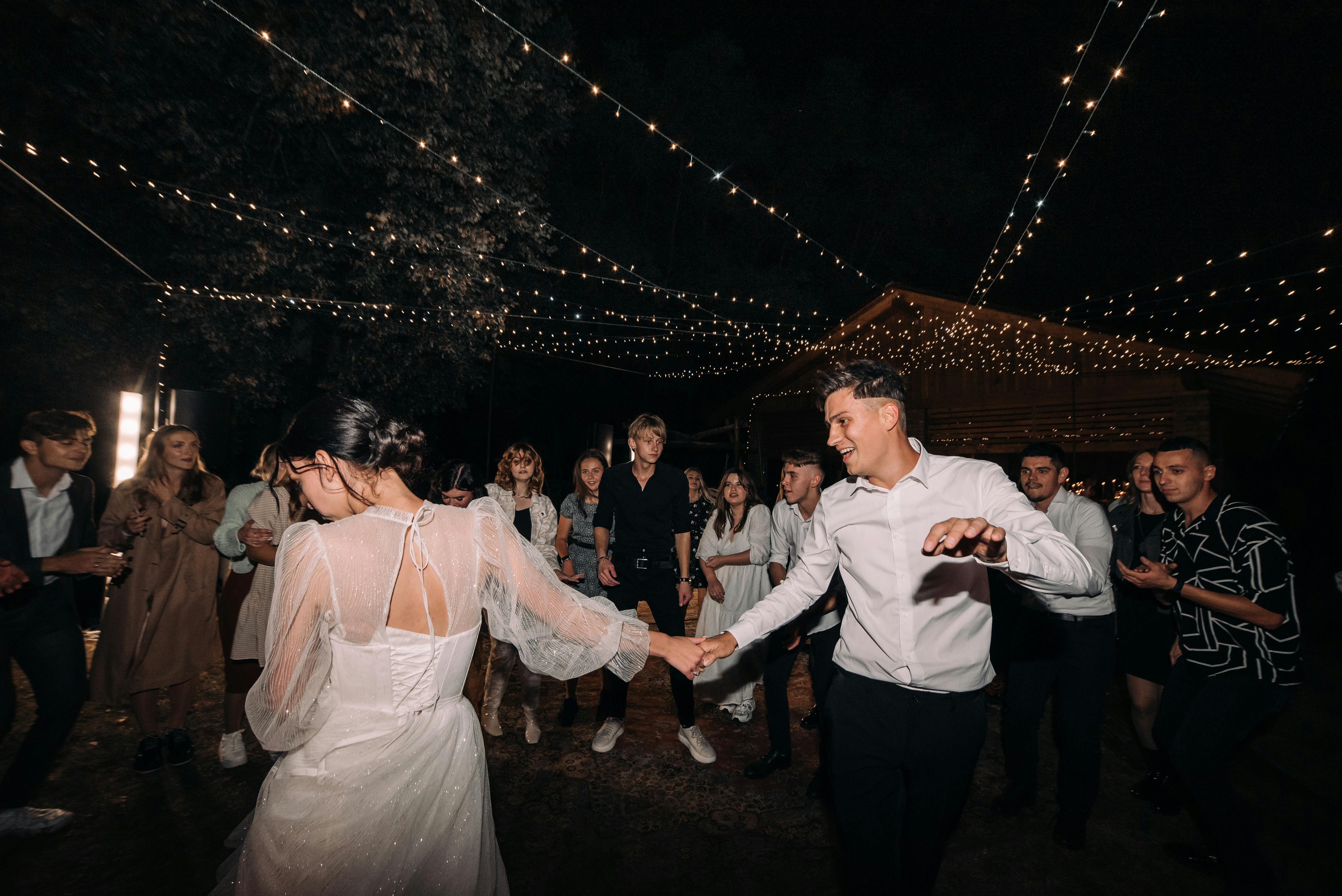 EDM at Weddings: How to Make Electronic Music Work - A couple dances joyfully under twinkling lights at an outdoor night wedding celebration.