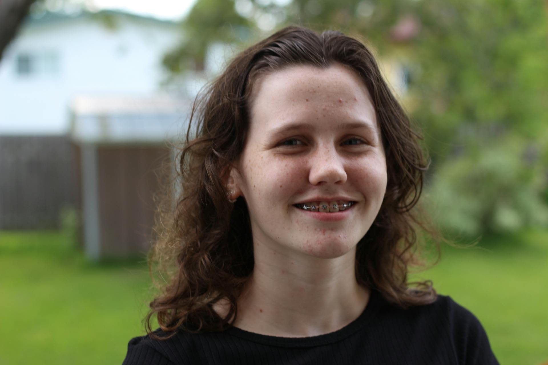 Close-up portrait of a smiling teenager with braces standing outside on a sunny day.