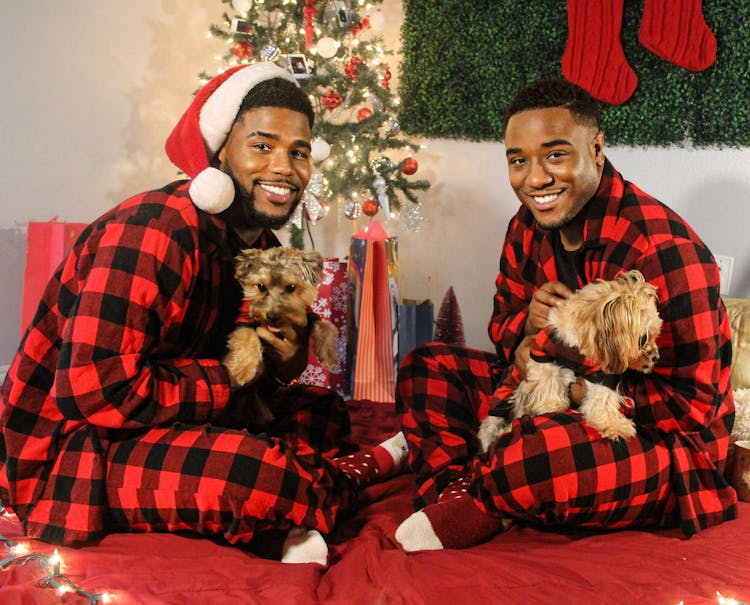 A Couple In Matching Pajamas Sitting By A Christmas Tree With Dogs 