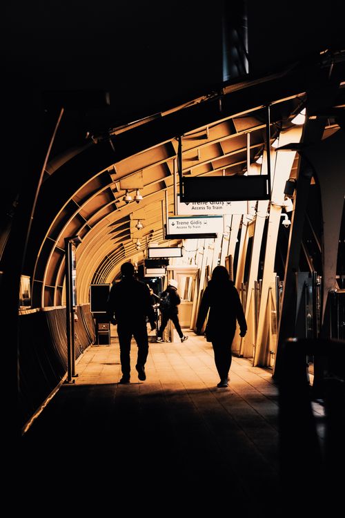 Free Silhouettes of people walking in a modern, illuminated train station tunnel. Stock Photo