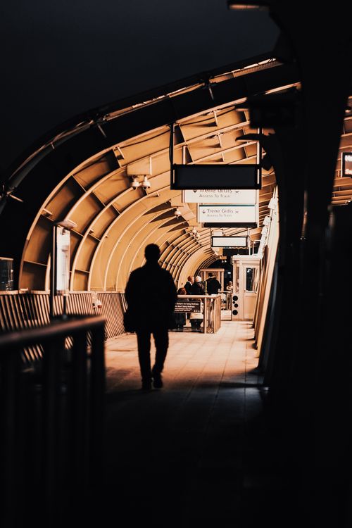 Free Silhouette of a person walking in a modern urban subway platform, showcasing architectural arches. Stock Photo