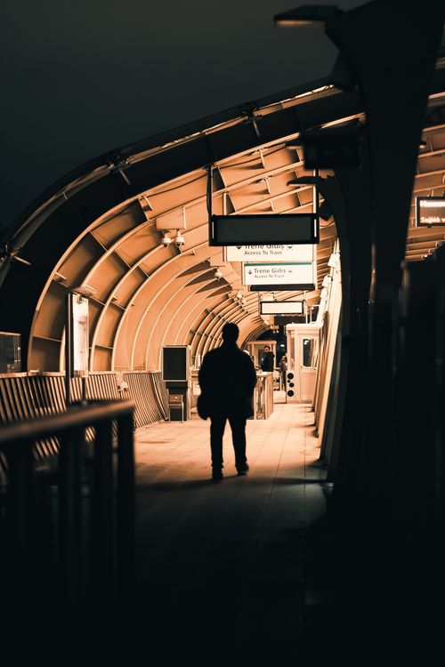 Free A lone silhouette stands in an illuminated transit station at night, capturing a mysterious urban atmosphere. Stock Photo