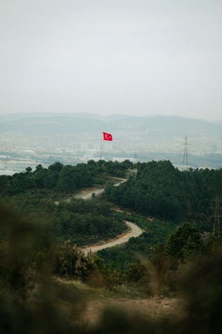 Discover scenic landscapes of İstanbul with a Turkish flag atop a hill, captured from above.