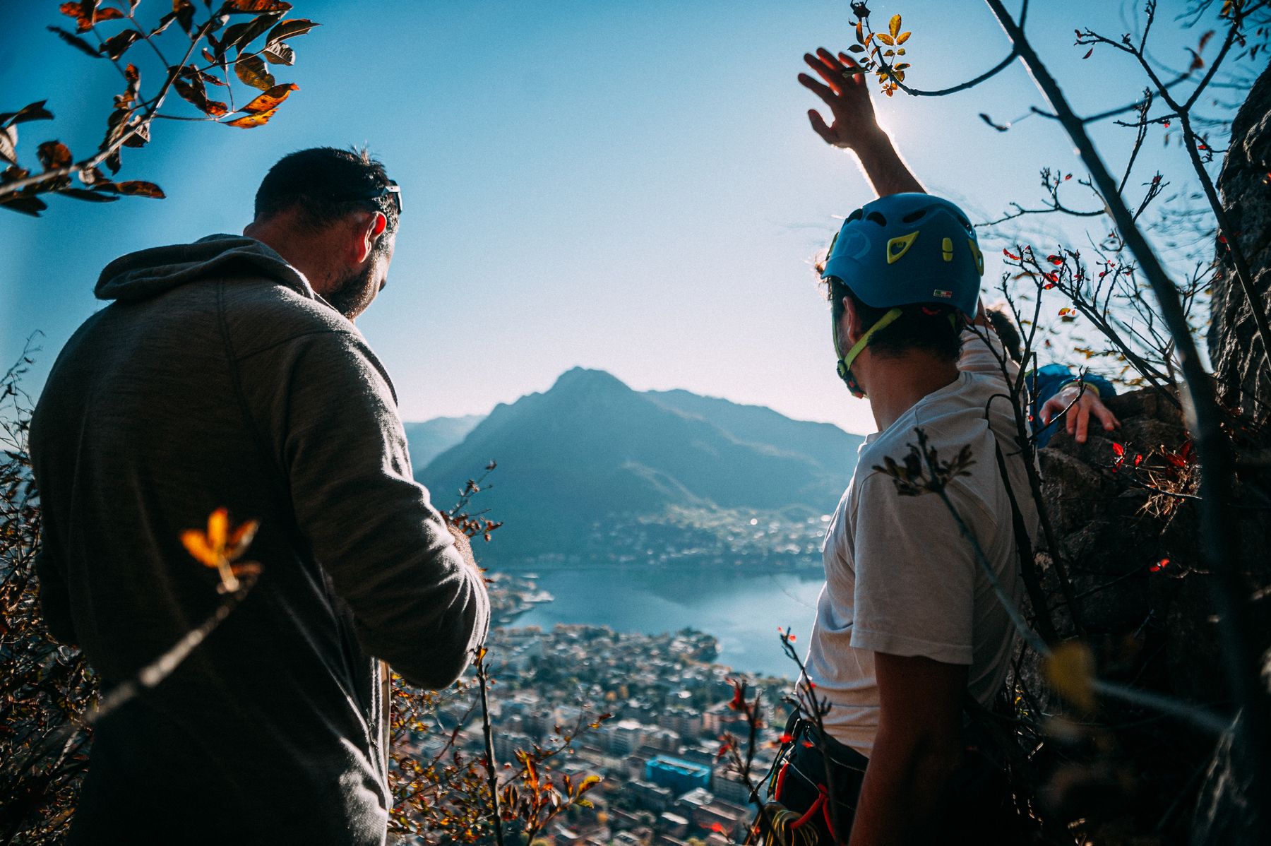 Two men climbing together above a mountain town